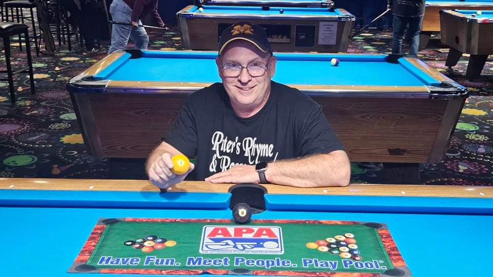 David Ritter kneeling next to a pool table after winning a pool tournament. 