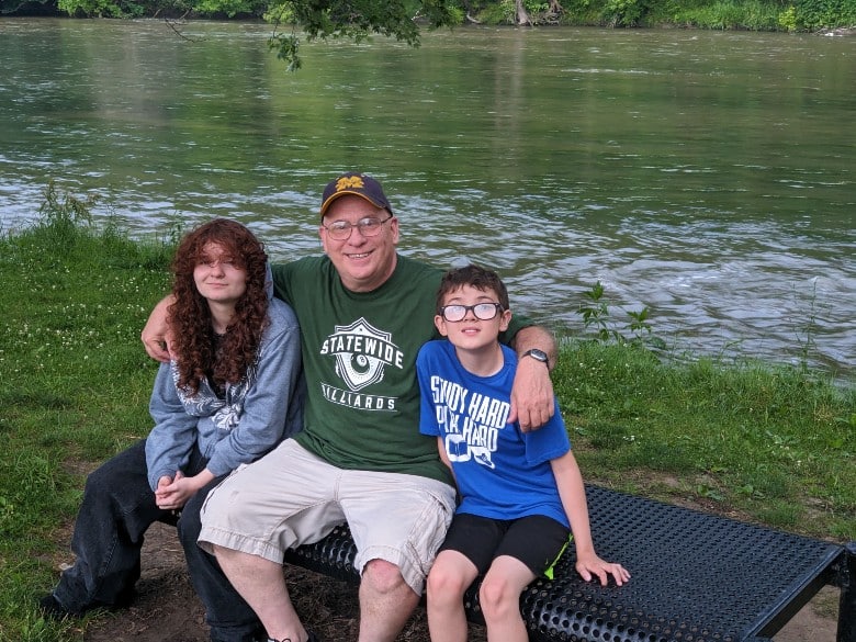 David Ritter sitting on a park bench next to Flint river with his grandkids 2024 